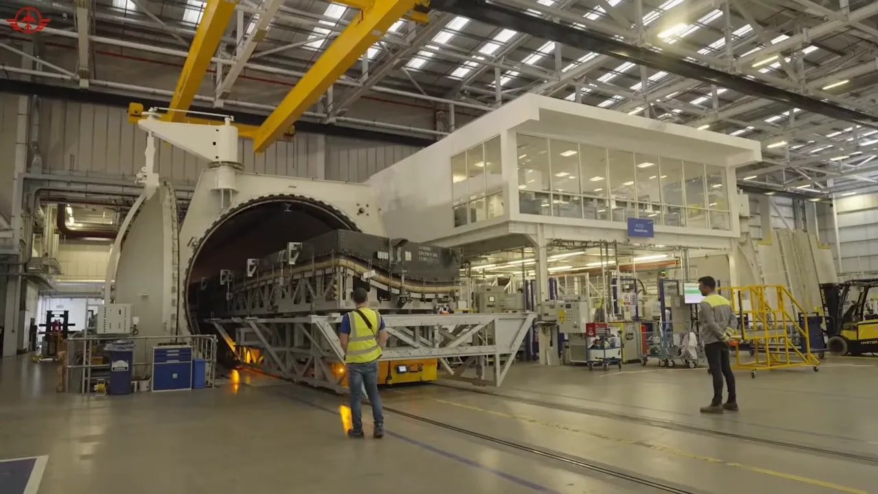 Large composite fuselage section mounted on industrial assembly tooling inside a factory