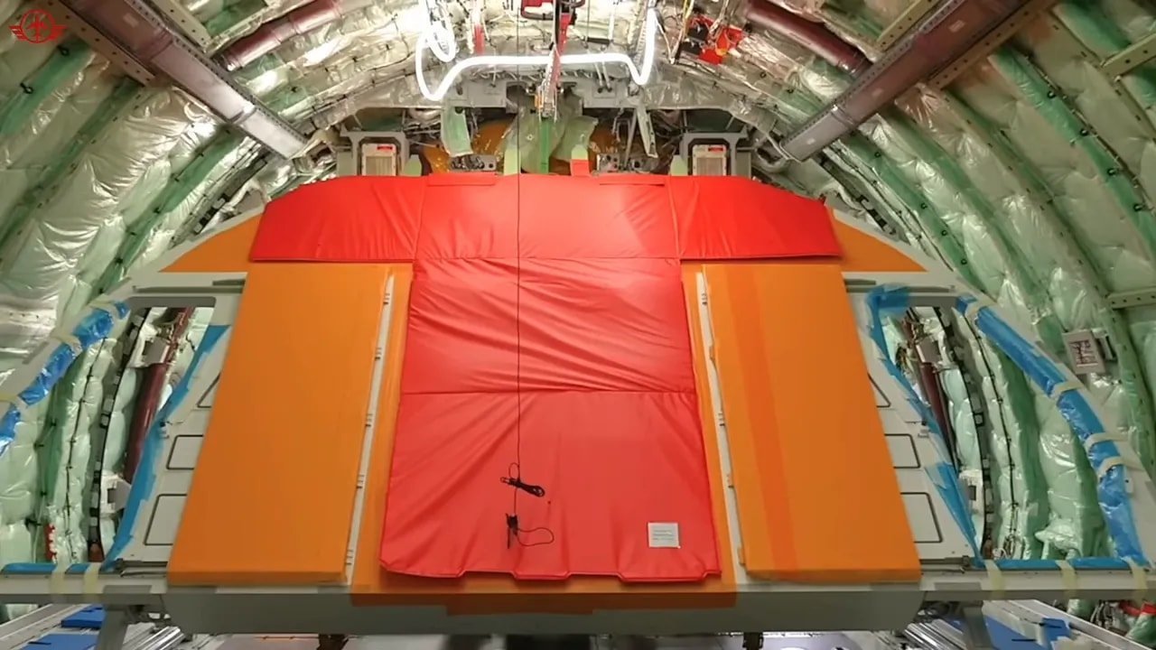Large red and orange main deck cargo door structure positioned inside an aircraft fuselage section